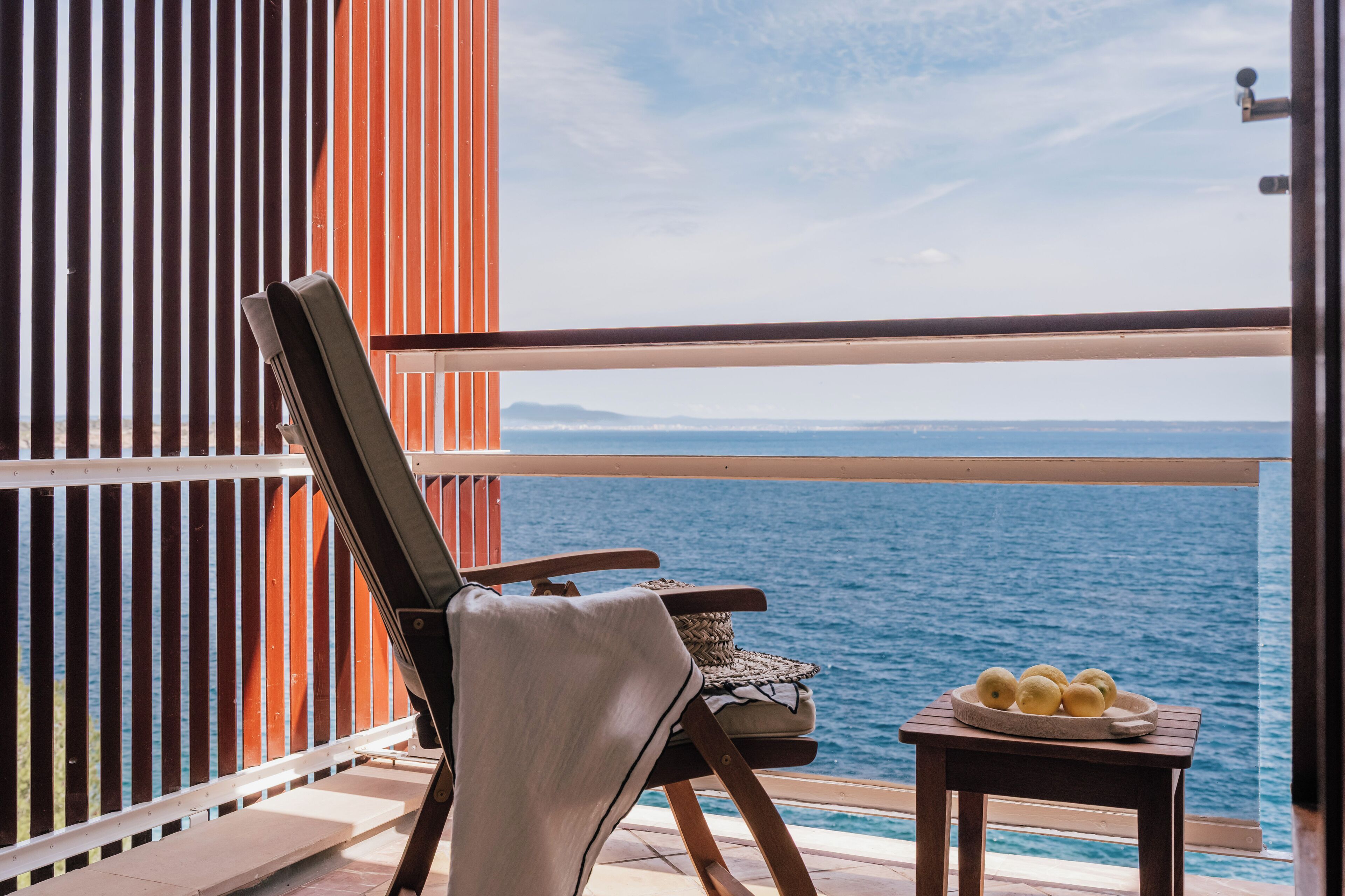 Un balcon avec vue sur la mer, une chaise, une petite table avec des citrons et une clôture en bois.