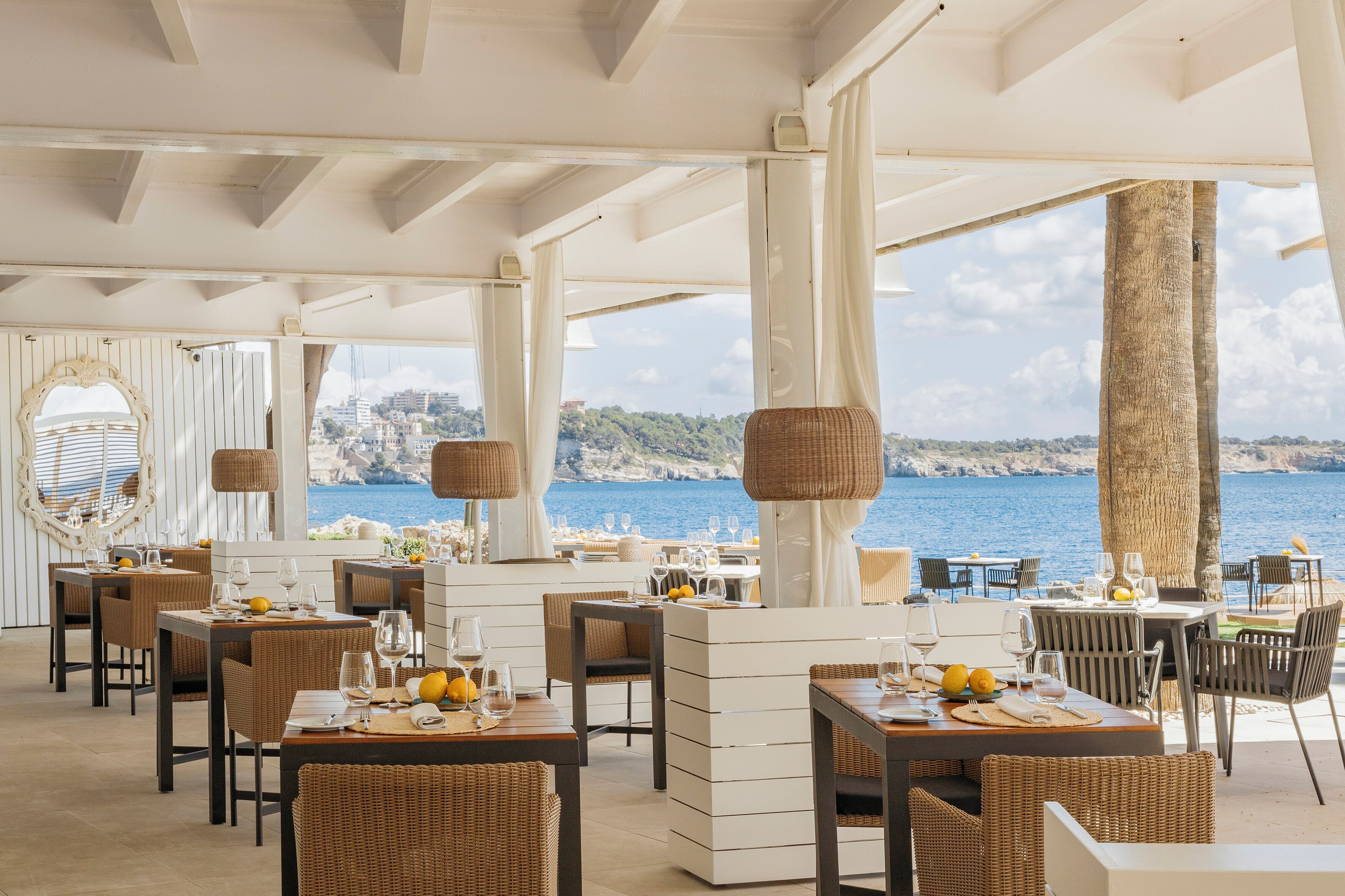 Un restaurante frente al mar con terraza, pilares blancos y vistas al océano.
