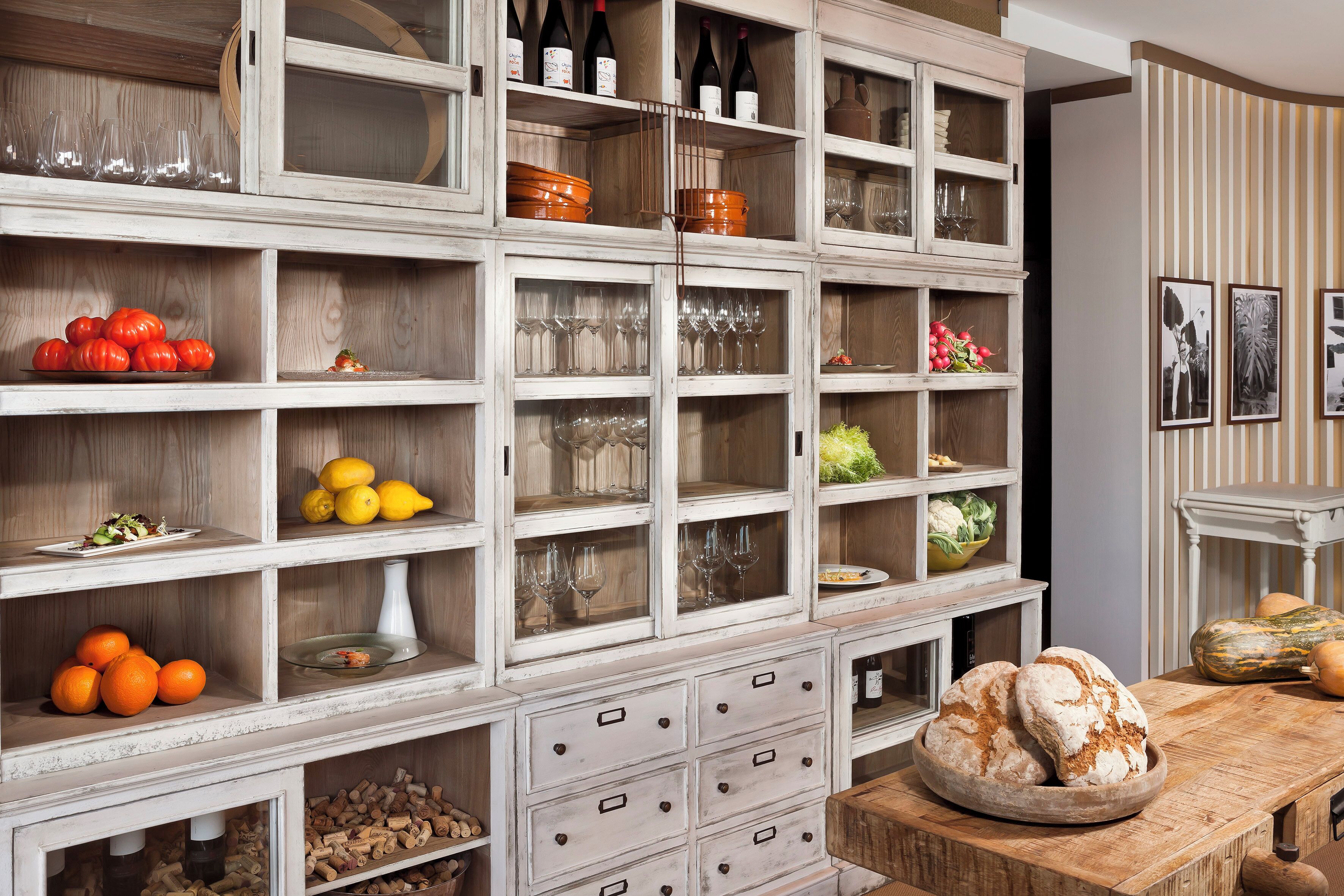 A wooden cabinet with multiple shelves containing wine bottles, glasses, and fruits.