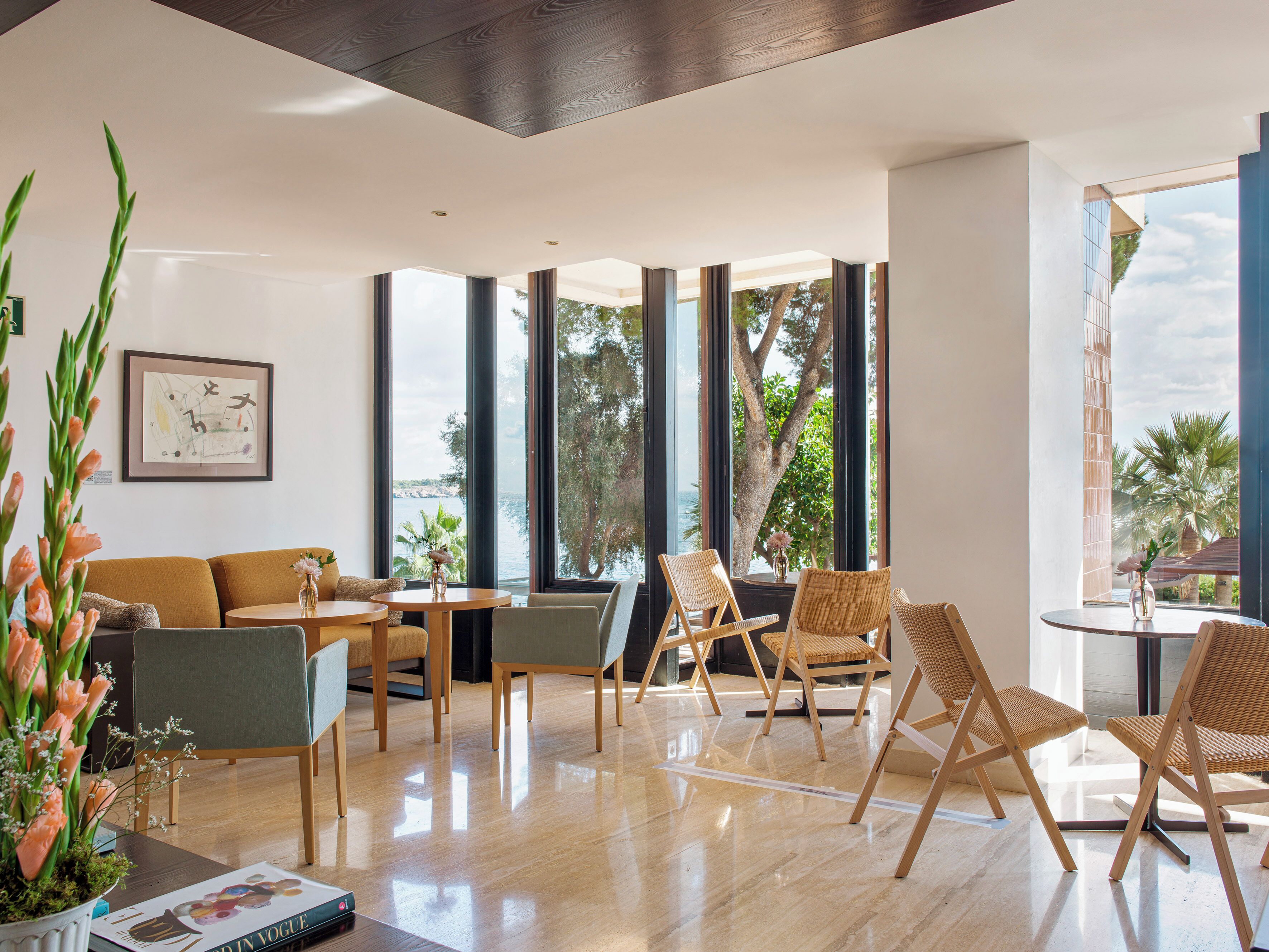 A modern living room with a sofa, chairs, a coffee table, and a view of the outdoors through large windows.