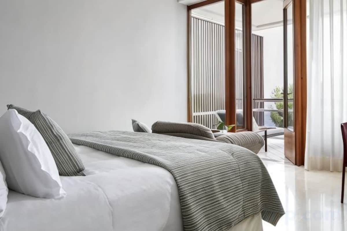 A bedroom with a large bed, a view of the outdoors, and a balcony.
