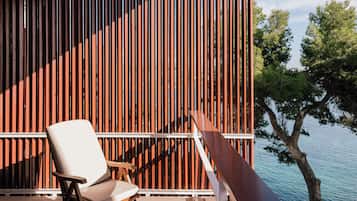 Una terraza de madera con una silla y una mesa, con vista a un cuerpo de agua y árboles.