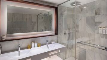 Un baño moderno con cabina de ducha de vidrio, un espejo grande y un tocador con dos lavamanos y encimera.