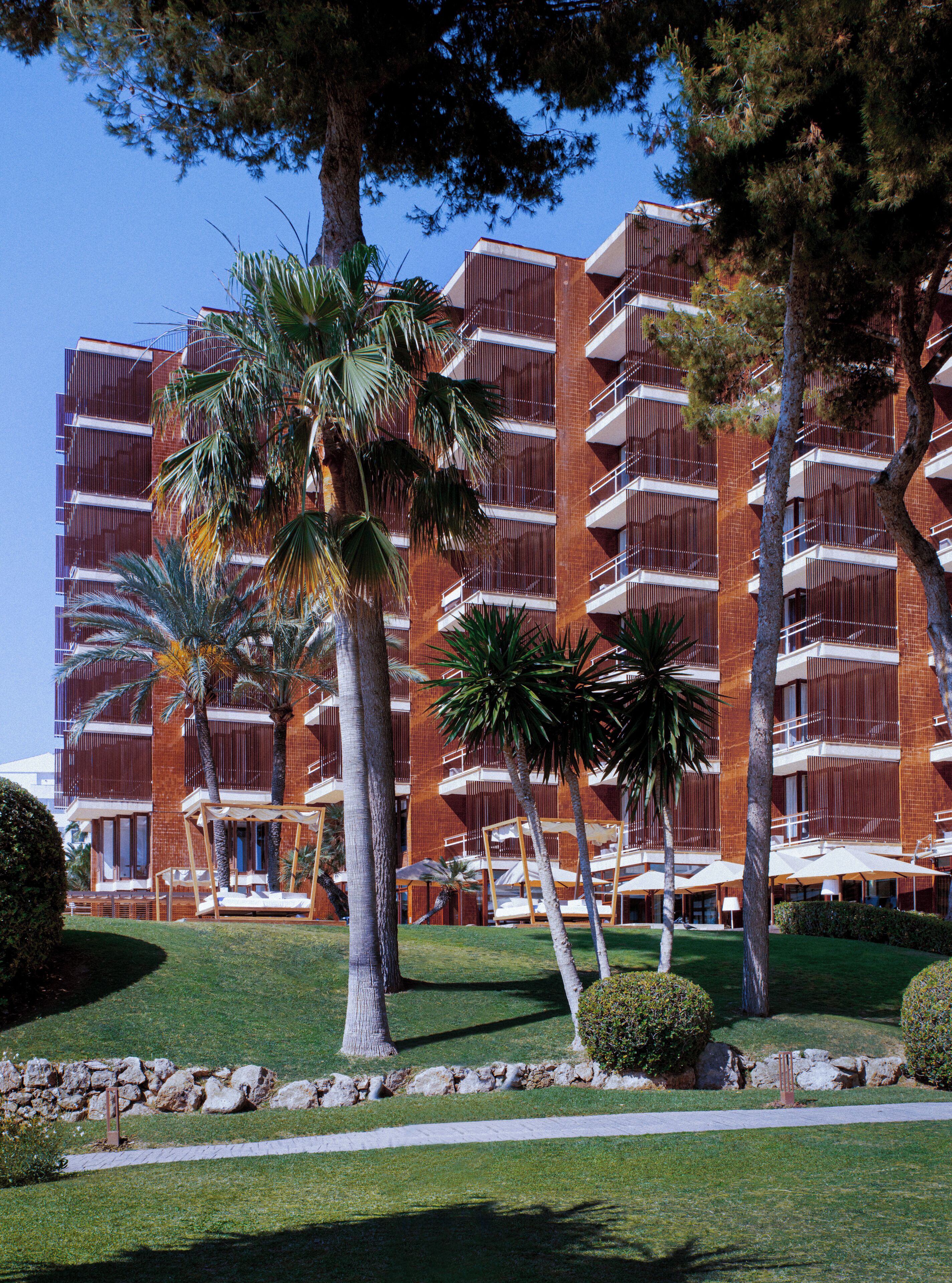 A multi-story hotel with balconies, palm trees, and a well-maintained lawn.