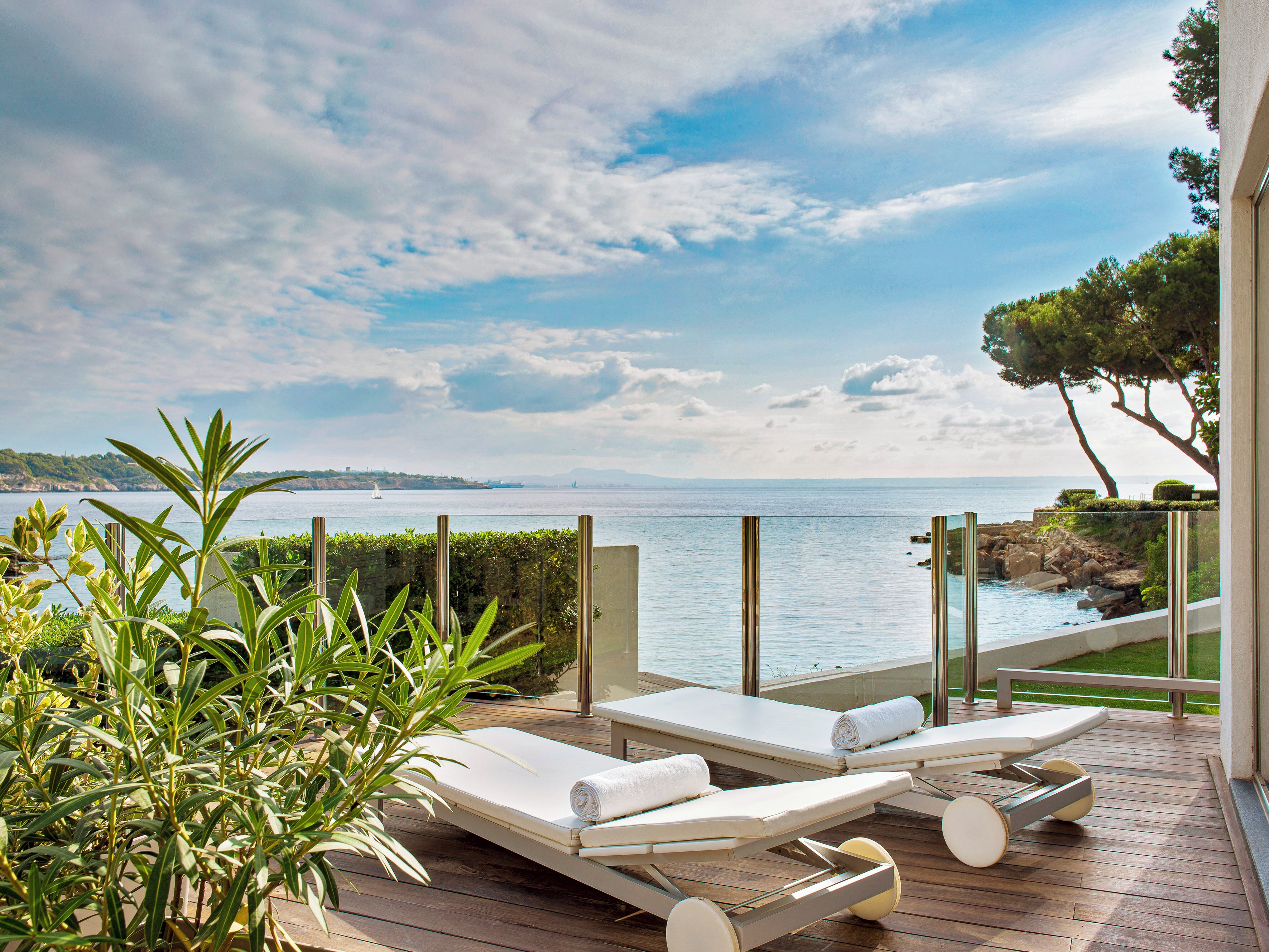 A deck with two sun loungers, a view of the sea, and a distant sailboat.