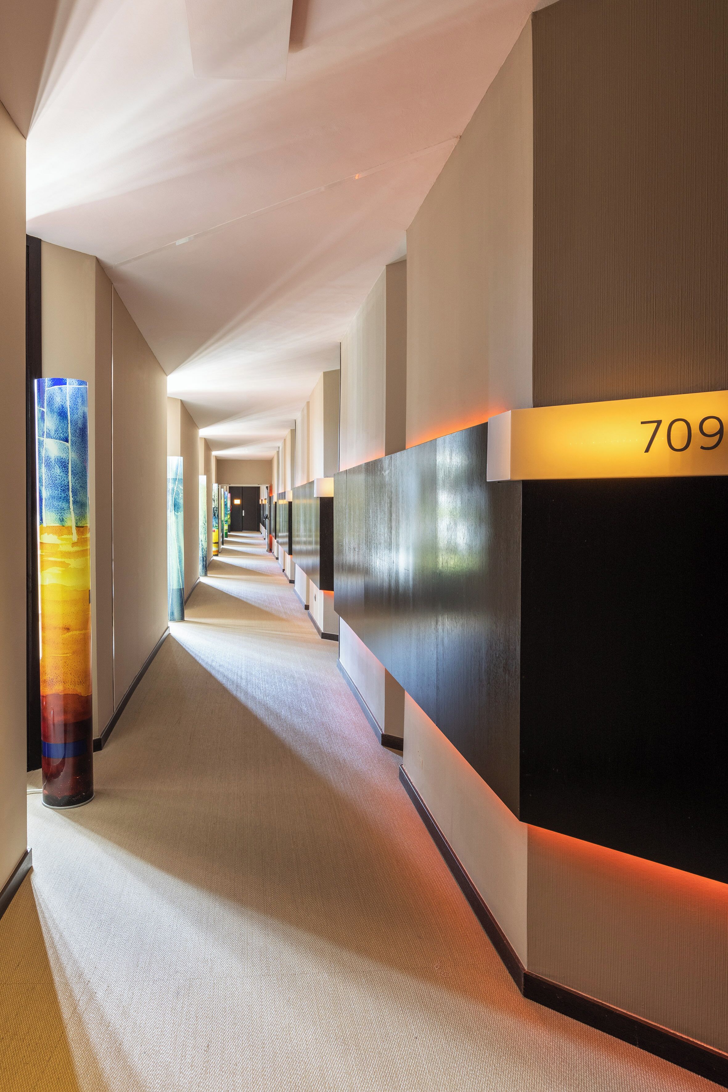A hotel corridor with a long, straight layout, a large pillar with a colorful design, and a number sign indicating room 709.