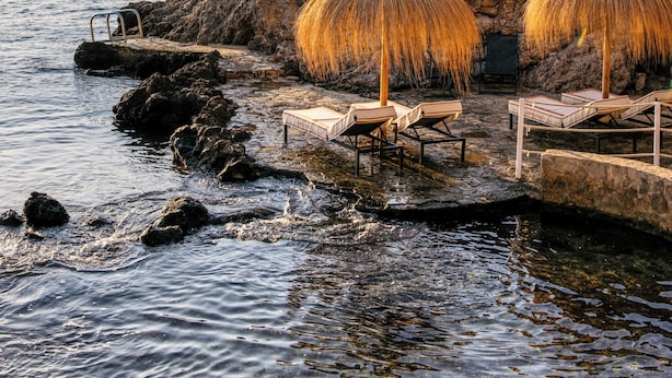 A coastal scene with thatched umbrellas and lounge chairs by the water. - Hotel de Mar Gran Meliá - The Leading Hotels of the World (Calvia)
