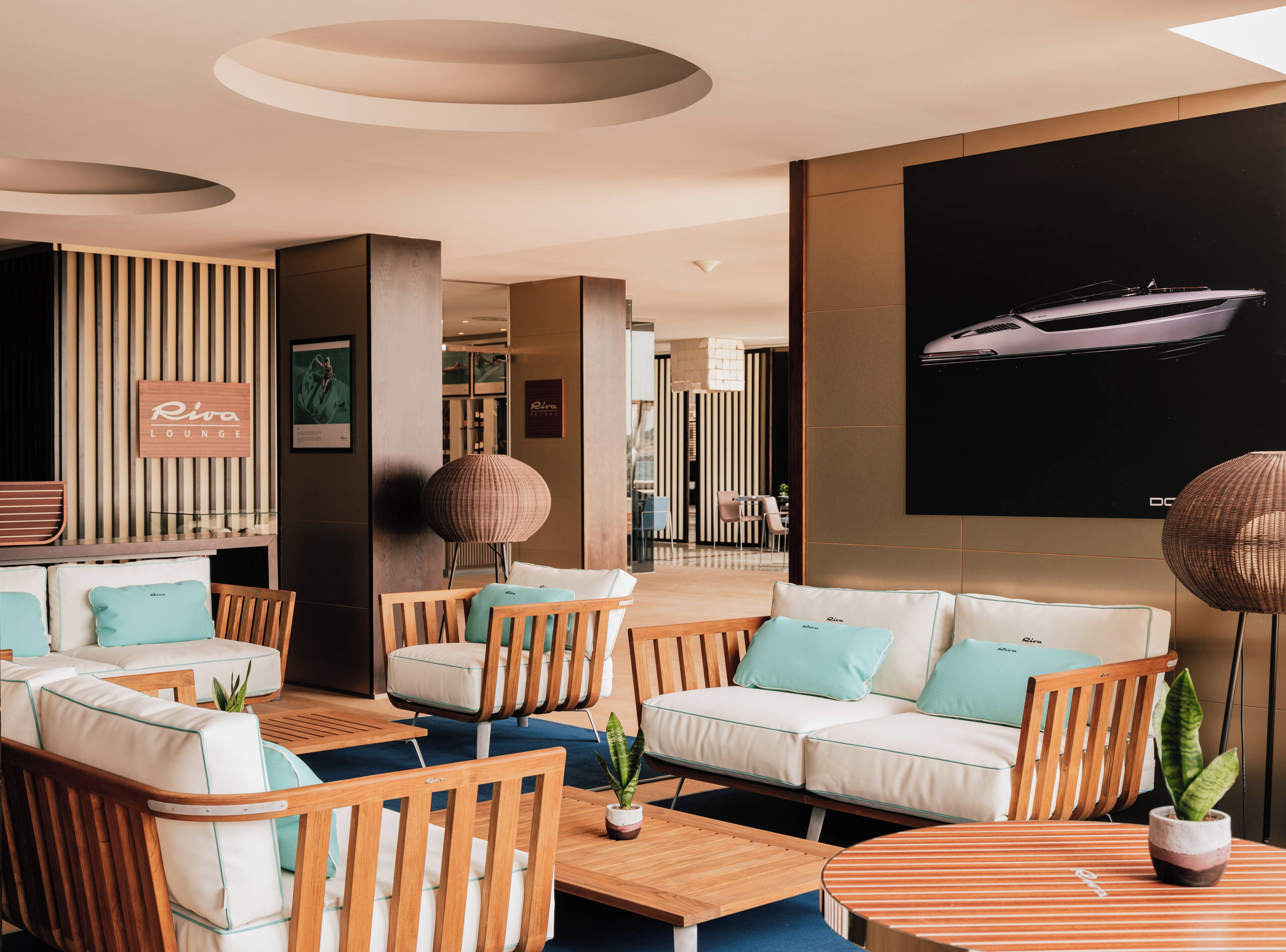 Un salon moderne avec des meubles en bois, un grand téléviseur fixé au mur et une enseigne indiquant « Riva Lounge ».