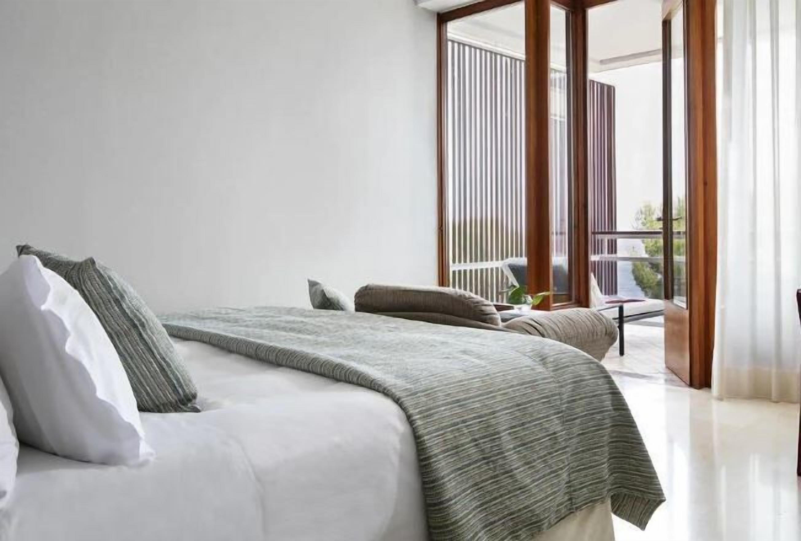 A modern bedroom with a large bed, a balcony with a view, and a sliding glass door.