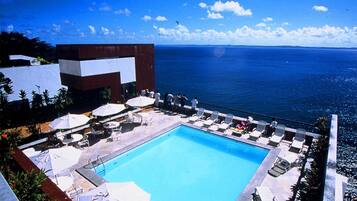 Zona de piscina con vista despejada al océano, rodeada de sillas de descanso y sombrillas.