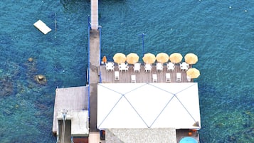 Een steiger die zich uitstrekt over helderblauw water, met een zonnedek met ligbedden en parasols, en een zwembad aan de zijkant.