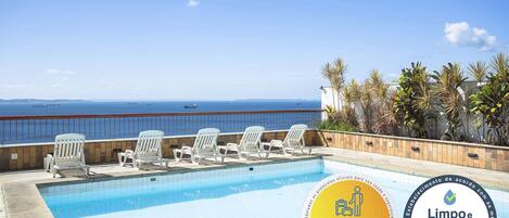 En pool med hvide stole og havudsigt.