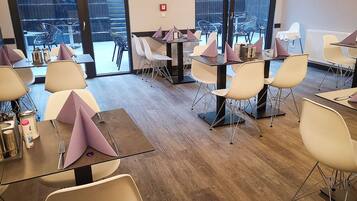 A modern dining area with tables and chairs, large windows, and a view of the outside.