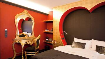 Ein Hotelzimmer mit einem großen Bett, einem spiegeln Spiegel mit goldener Rahmung, einem Schreibtisch und einer Wand in roter Farbe.