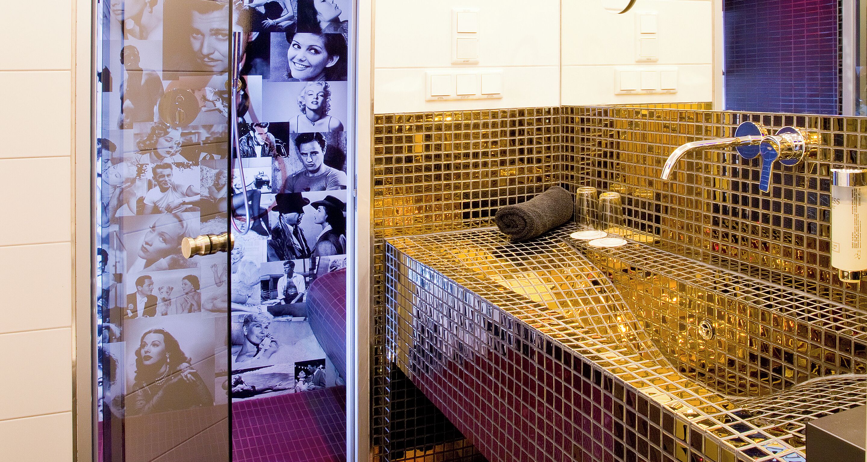 A bathroom with a golden mosaic wall, a bathtub with a towel, and a mirror with photos.