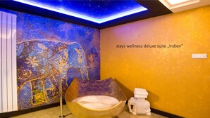 Een wellnessruimte met een sterrenhemelplafond, een grote decoratieve wand, een stenen bad en een klein beeldje.