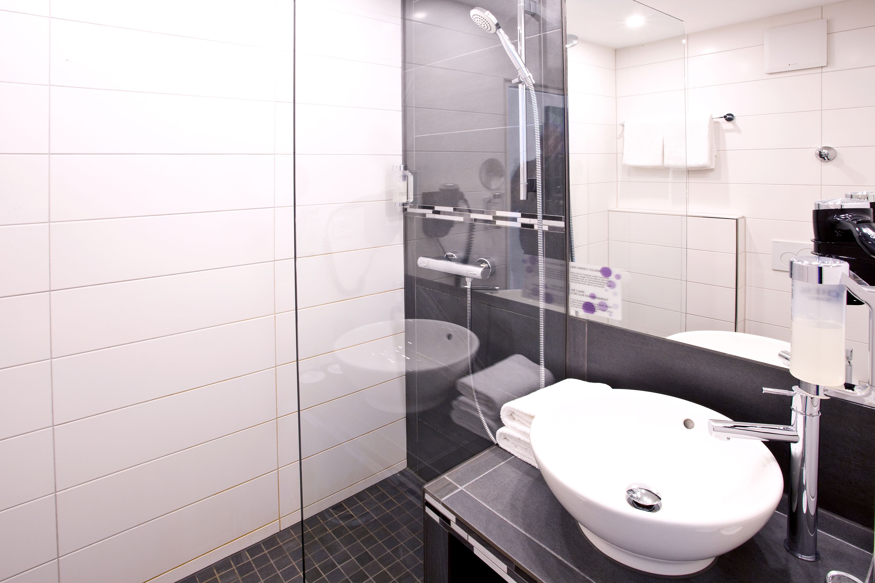 Un baño moderno con ducha envuelta en vidrio, un lavamanos blanco y una encimera negra.