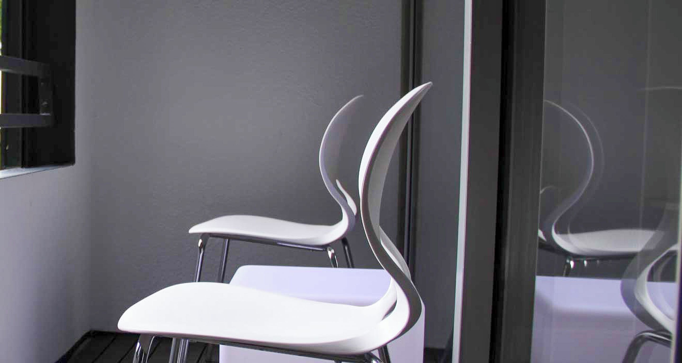 A modern chair with a sleek, curved design, positioned against a dark wall with a reflective surface.