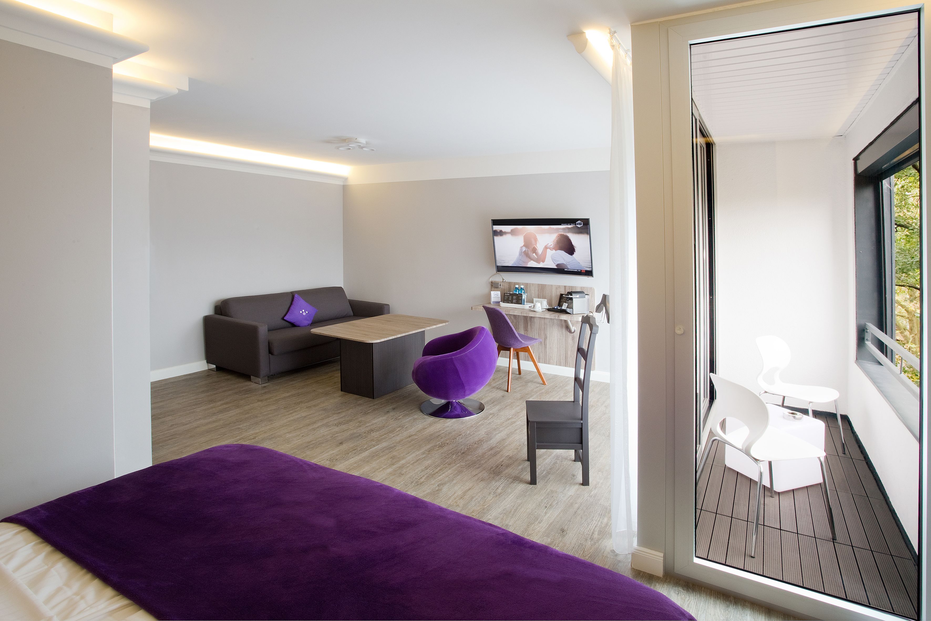 Ein modernes Hotelzimmer mit einem Bett, einem Schreibtisch, einem Sessel und einem Fernseher.