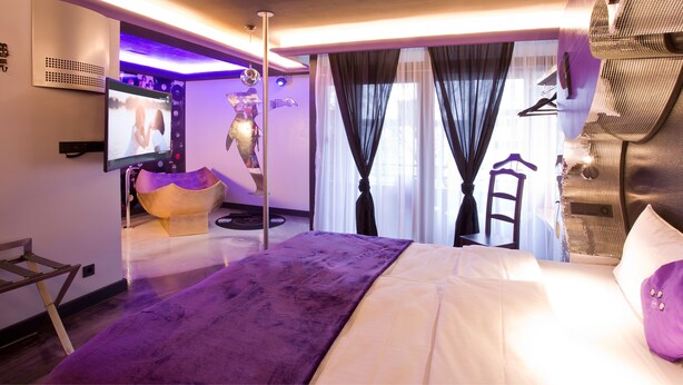 Een moderne hotelkamer met een groot bed, een flatscreen televisie, een uniek kunstwerk aan de muur en een zithoek met een paarse bank.