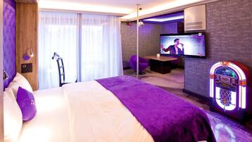 Una habitación de hotel moderna con una cama grande, televisión, juke box y un área de descanso con mesa y sillas.