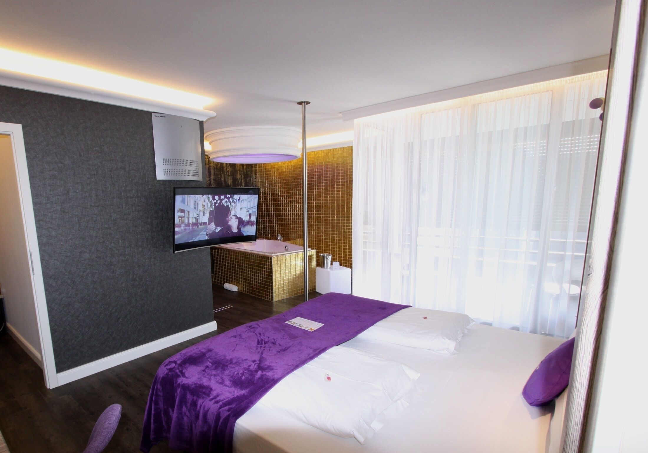 Una habitación de hotel con cama, televisión, baño y ventana con cortinas.
