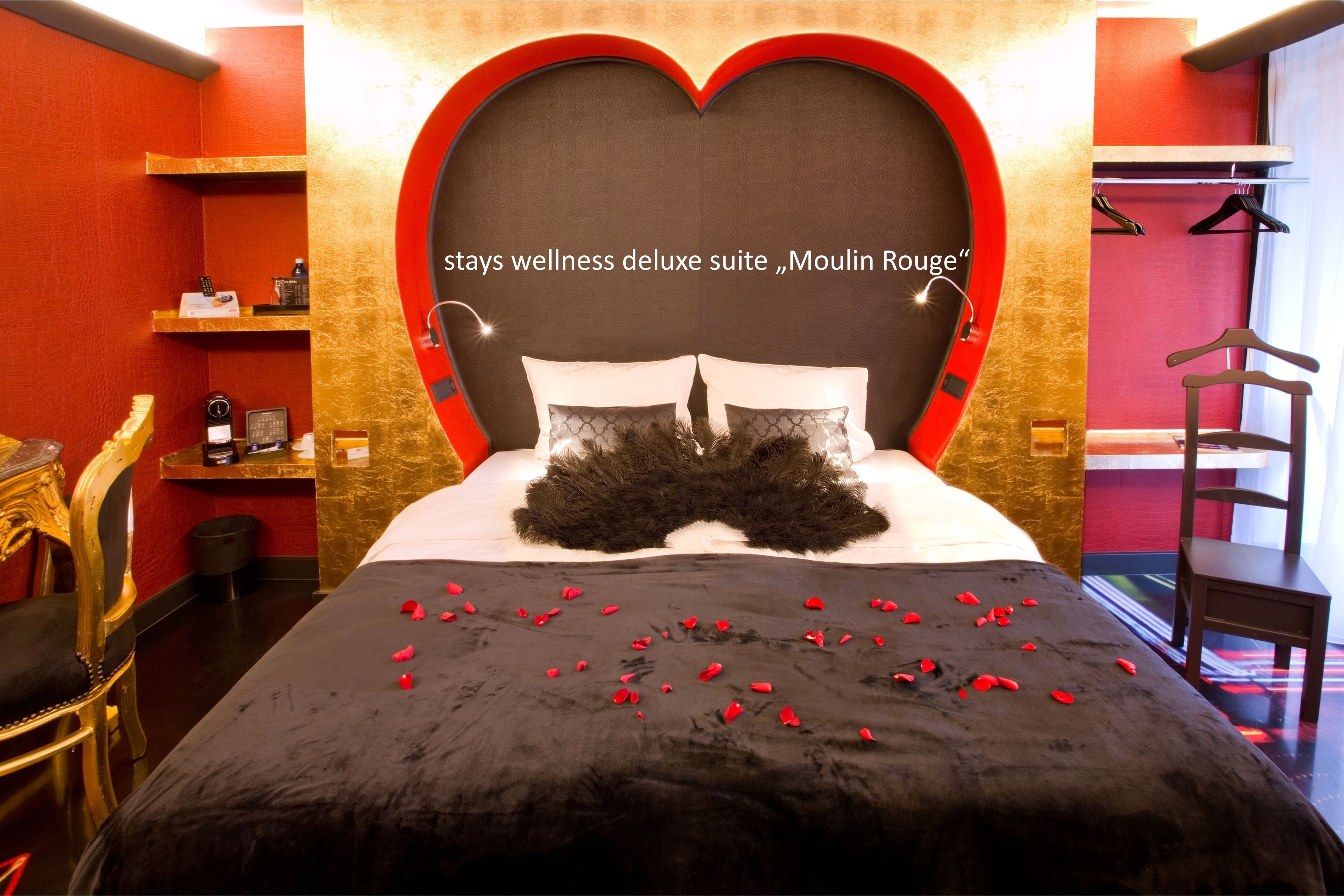 A bed with rose petals, a heart-shaped headboard, and a minibar.