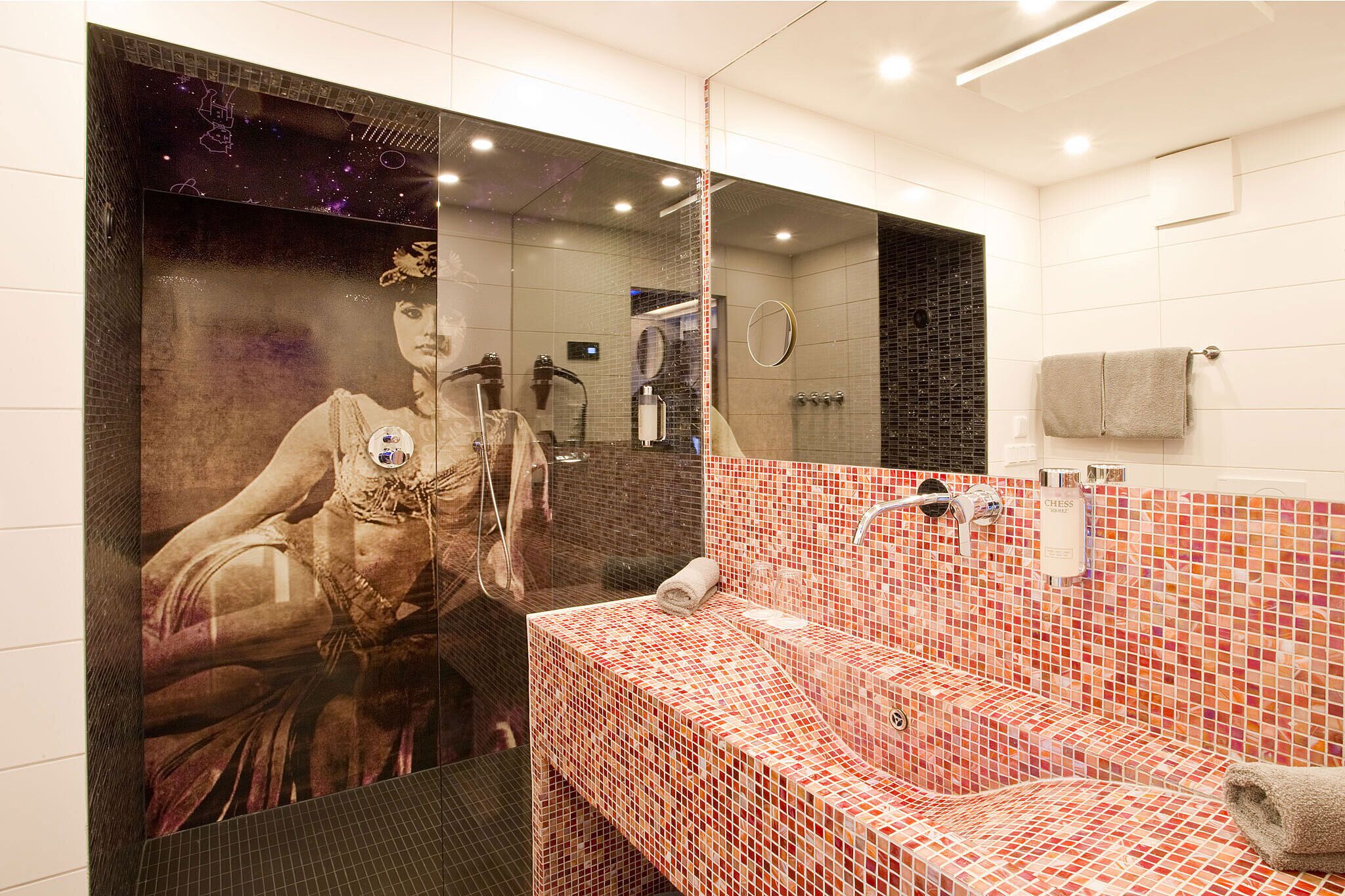 A modern bathroom with a large mirror, a red-tiled sink, and a shower area.