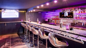 Een bar met een lange toonbank, meerdere stoelen en een televisiescherm waarop een sportevenement wordt uitgezonden.