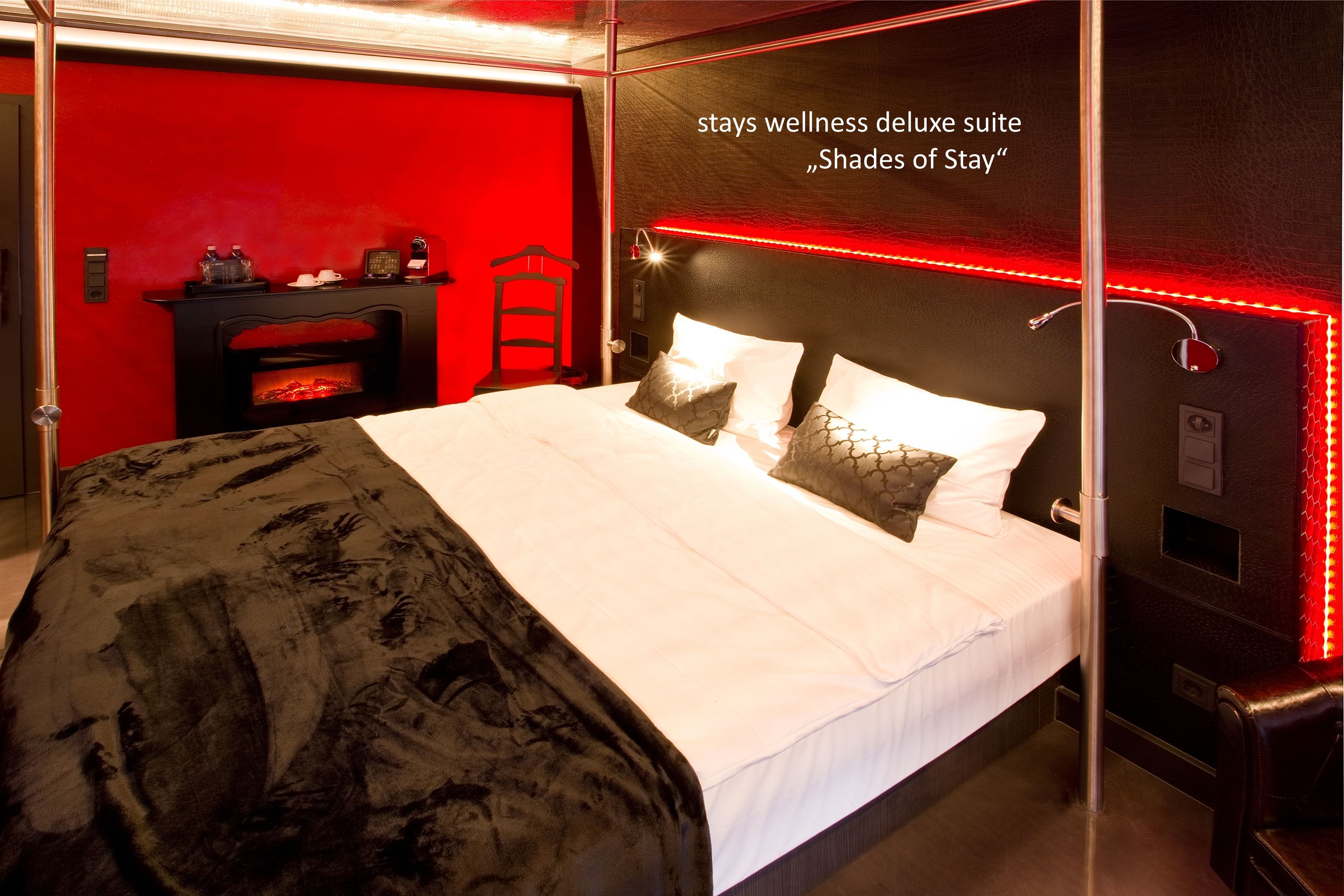 Hotelkamer met een rode accentmuur, een open haard, een bed met witte beddengoed en een rode lichtstrip.