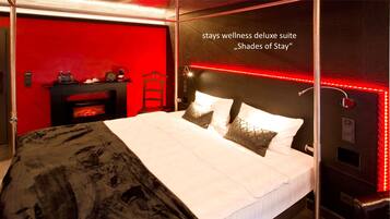 Hotelkamer met een rode accentmuur, een open haard, een bed met witte beddengoed en een rode lichtstrip.