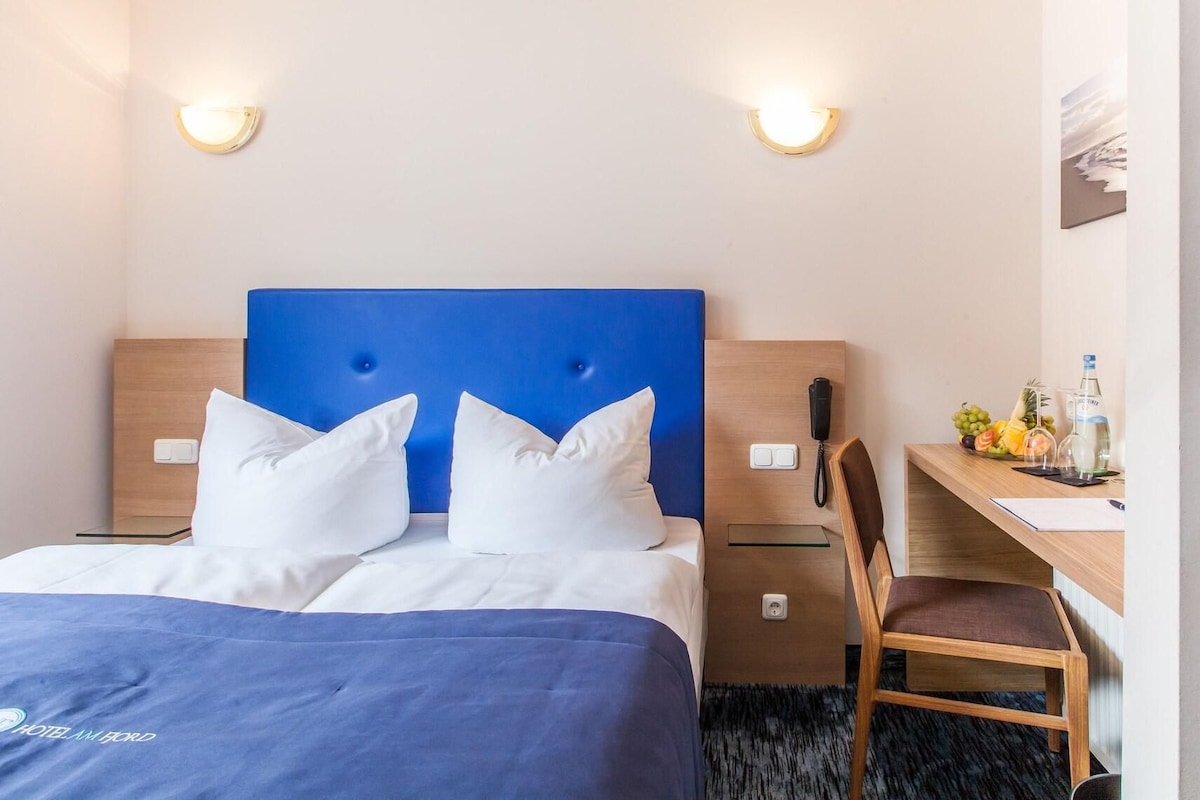Habitación de hotel con cama, escritorio, silla, teléfono y frutero.