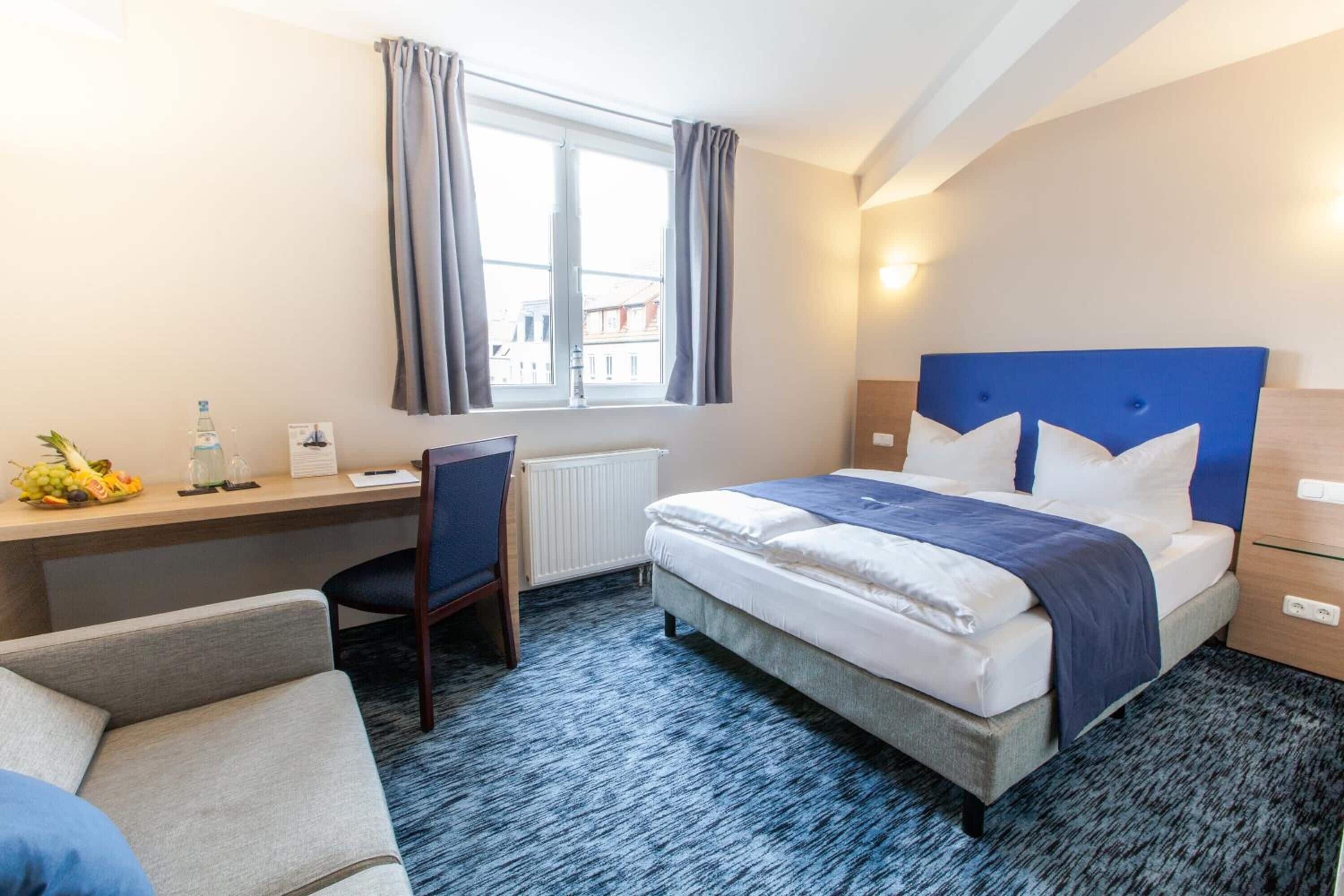 A hotel room with a bed, a desk, a chair, and a window with curtains.