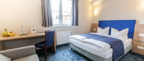 A hotel room with a bed, a desk, a chair, and a window with curtains.