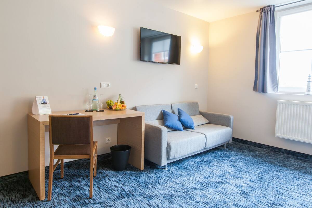 A hotel room with a desk, chair, and a grey sofa with blue cushions.
