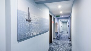 A hotel hallway with a sailboat painting on the wall, a carpeted floor, and a ceiling light.