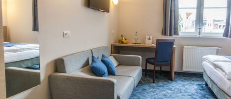 A hotel room with a sofa, a desk, a chair, a bed, a TV, and a window with curtains.