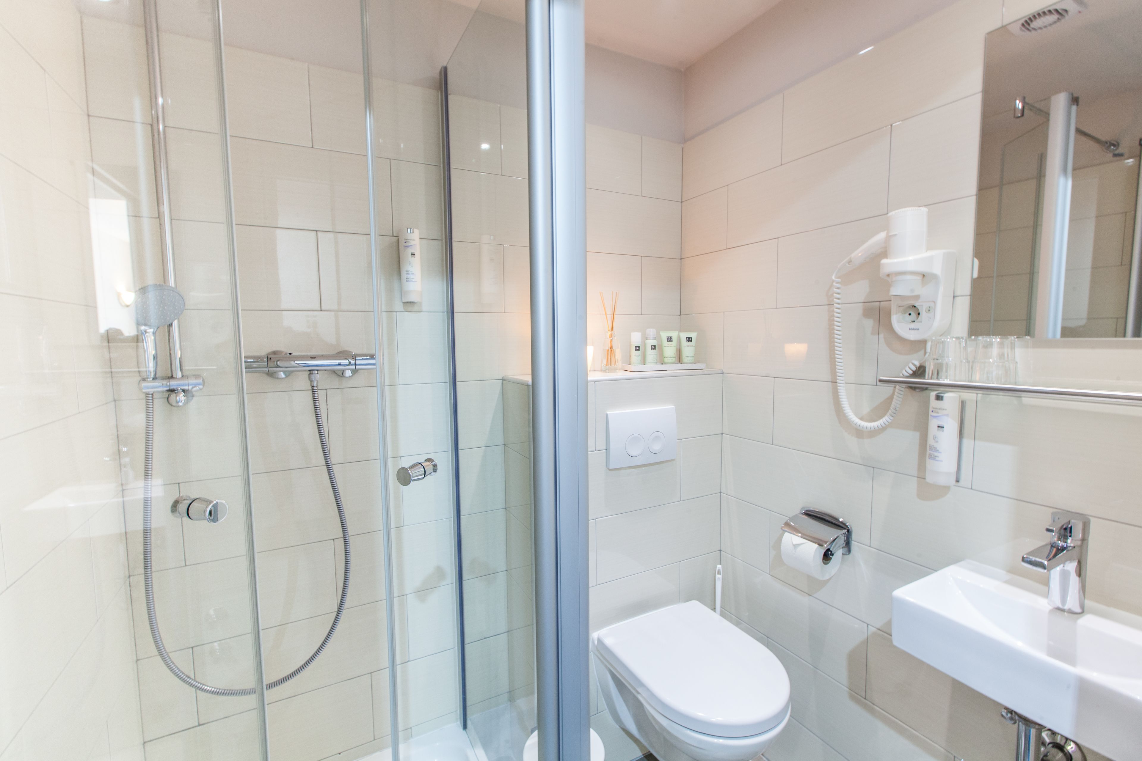 Une salle de bain moderne avec une douche à parois de verre, des toilettes blanches, un lavabo et un miroir.