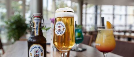 A bottle of pilsner beer, a glass of pilsner beer, and a cocktail on a wooden table.