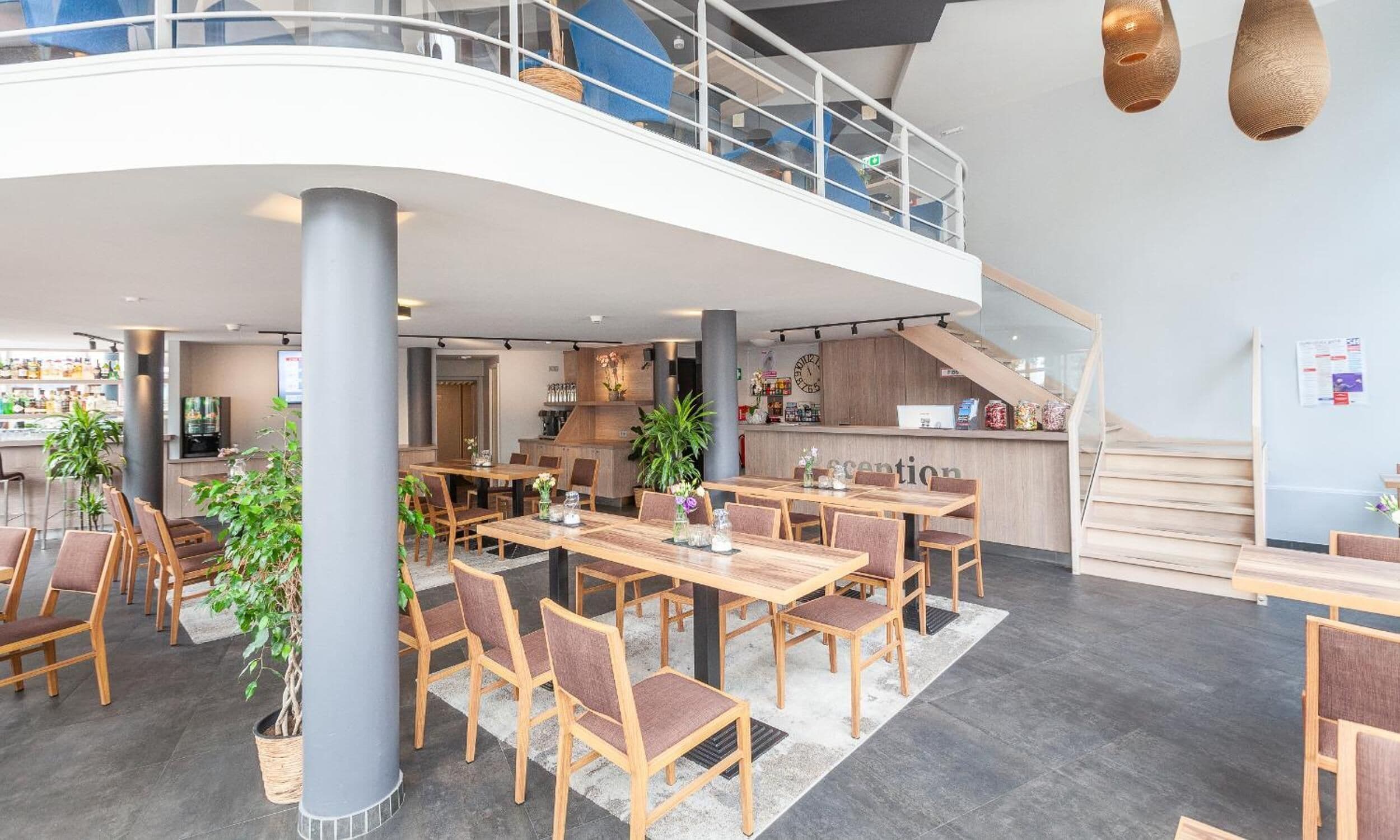 A spacious indoor area with multiple wooden tables and chairs, a staircase, and a reception desk.