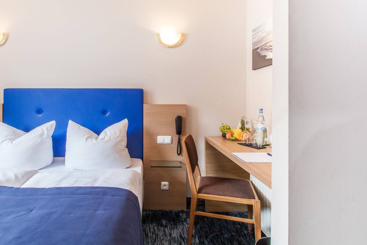A hotel room with a bed, a desk, a chair, a phone, and a fruit basket.