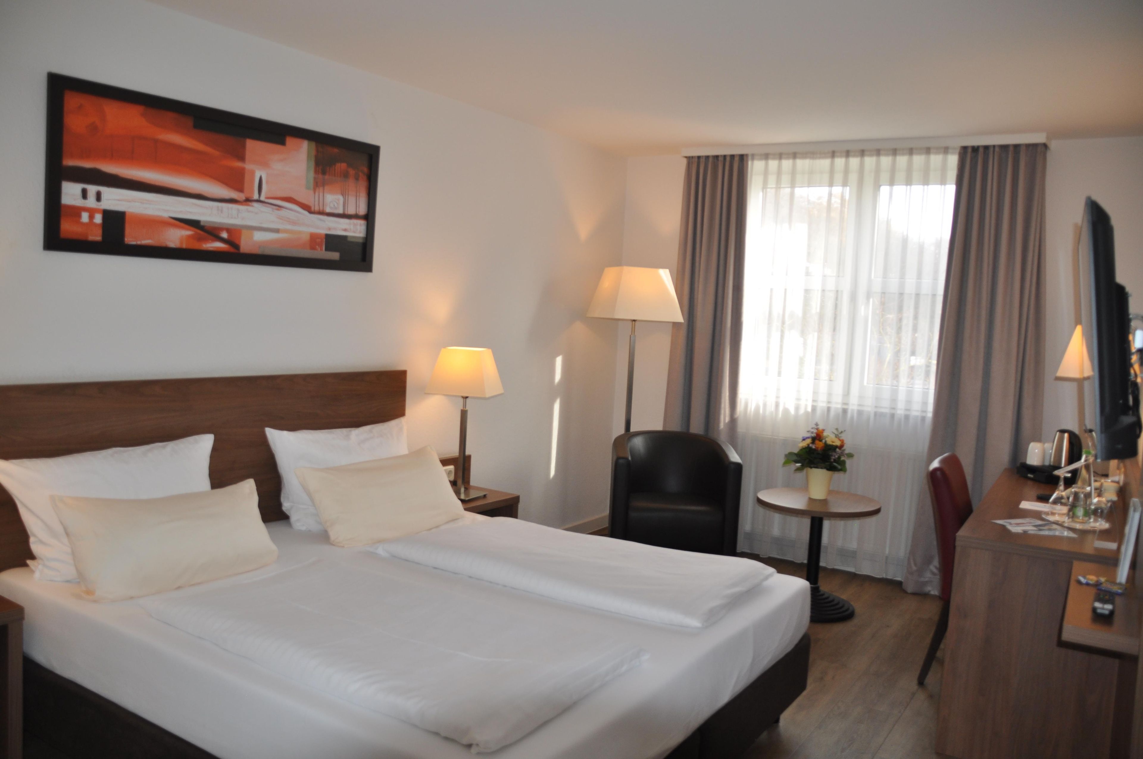 Habitación de hotel con una cama grande, dos lámparas de noche, un escritorio con una silla, una mesita con lámpara y un cuadro en la pared.