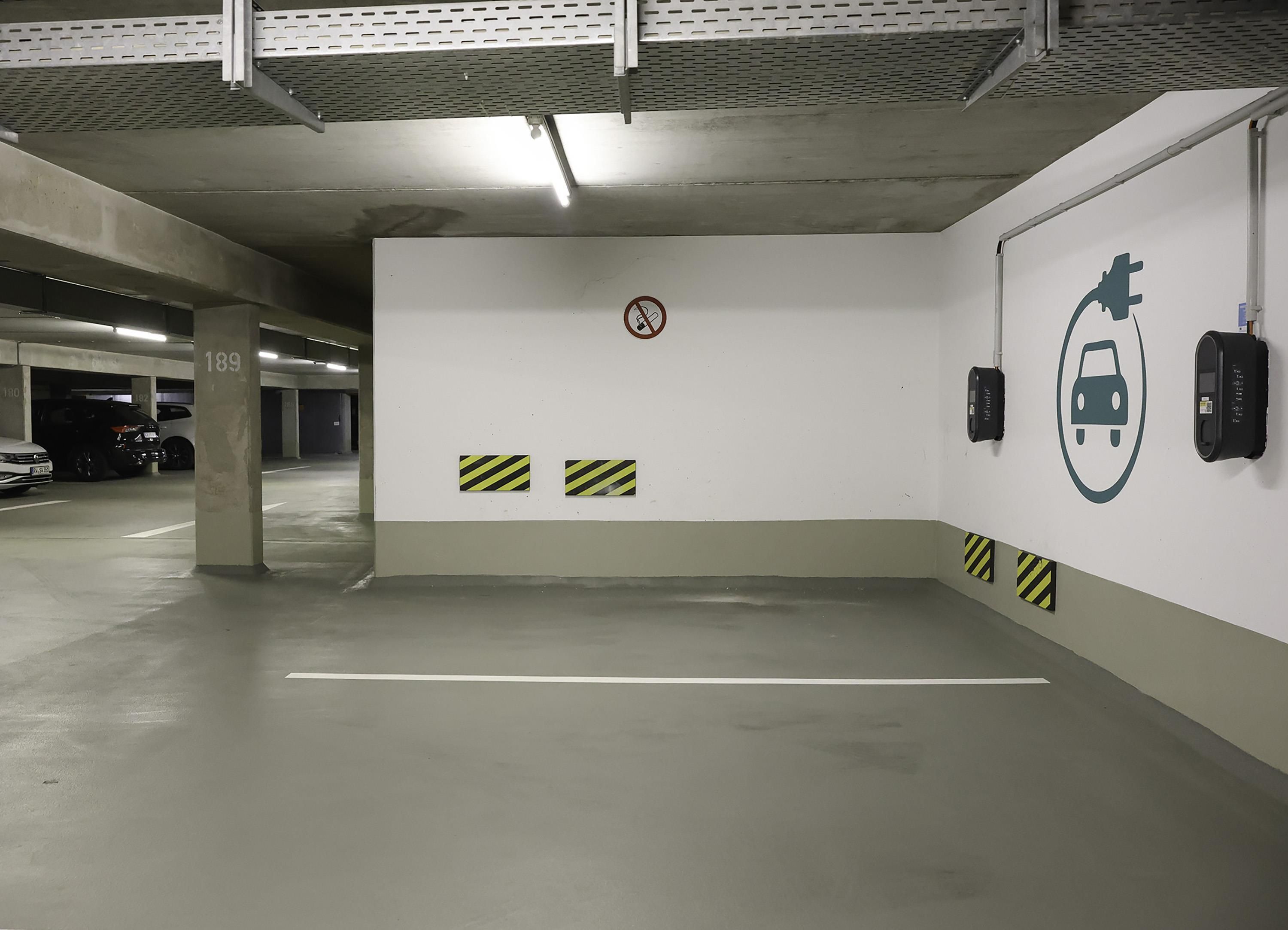 A parking garage with concrete pillars, a no-smoking sign, and electric vehicle charging stations.