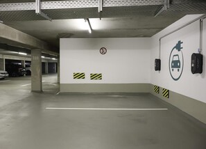 Un garaje para estacionar con pilares de hormigón, un cartel de prohibido fumar y estaciones de carga para vehículos eléctricos.