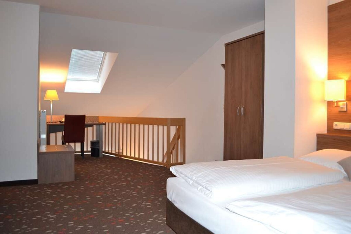 A hotel room with a bed, a desk with a chair, a wardrobe, and a window with a view of the outside.
