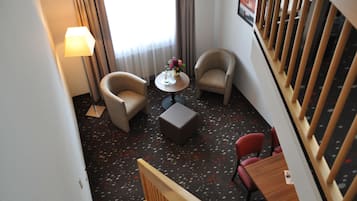 A hotel room with a bed, a desk, two armchairs, a small table with a vase of flowers, and a window with curtains.