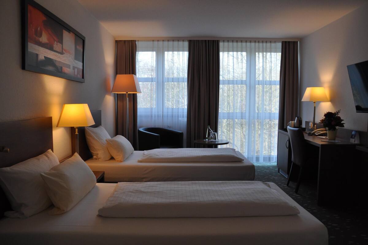 A hotel room with two beds, a desk, a chair, and a TV.