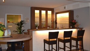 Zona de bar con mostrador, dos taburetes y un mueble de vidrio con botellas.