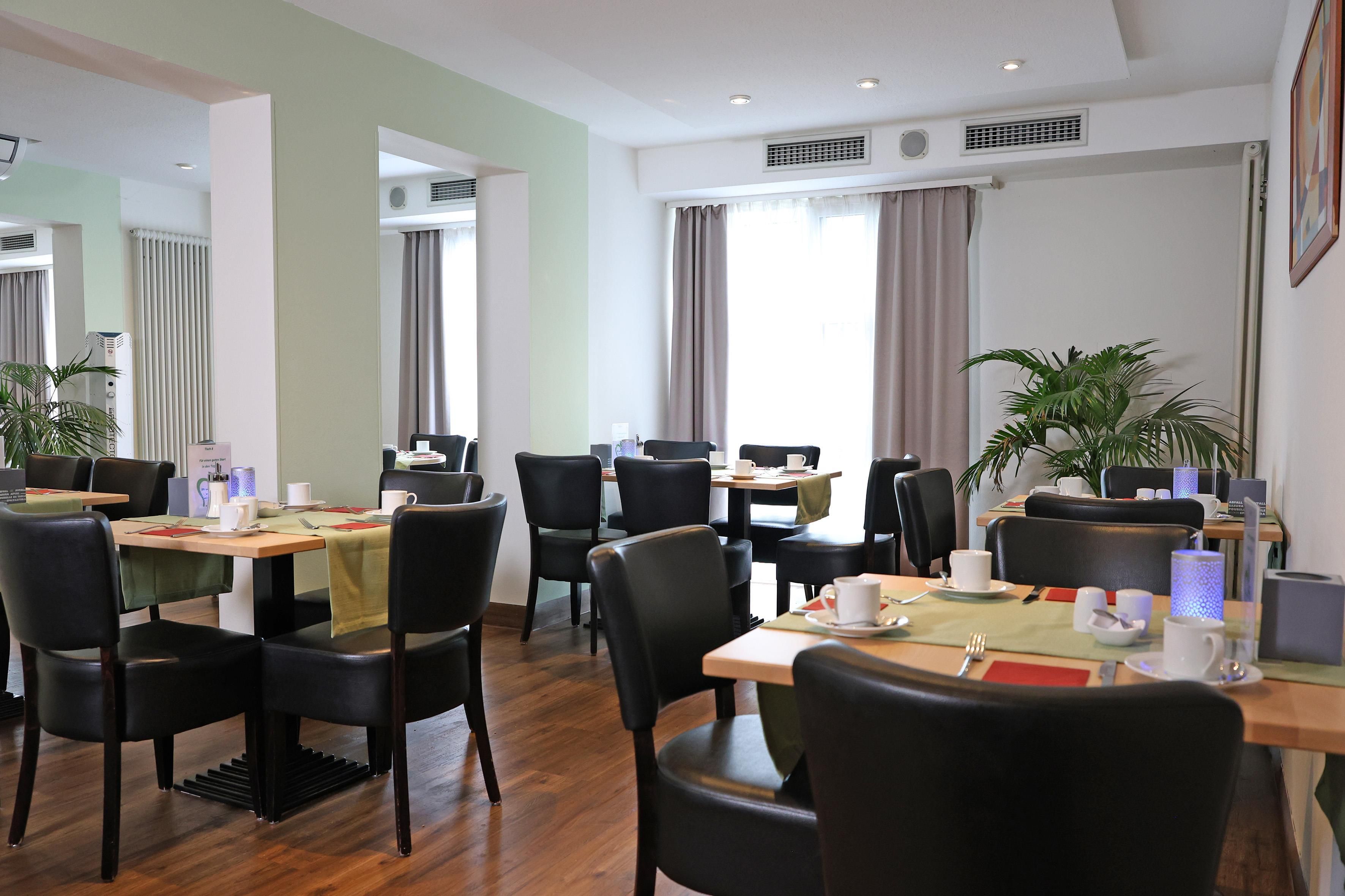 Un comedor de hotel con varias mesas y sillas, dispuesto con vajilla y una planta en maceta.