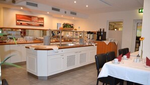 Un restaurante con una barra central, armarios blancos y un comedor con mesas dispuestas para el servicio.